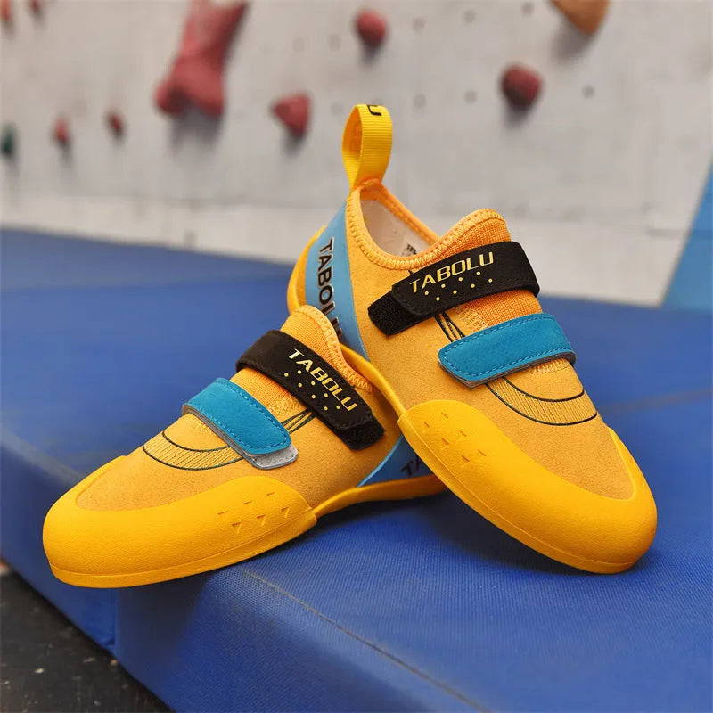 Beginner rock climbing shoes with Velcro strap in black and red colour scheme on a rocky surface.