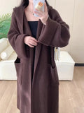 A long, loose grey hooded cardigan coat for women on a hanger, showing its length and raglan sleeves.