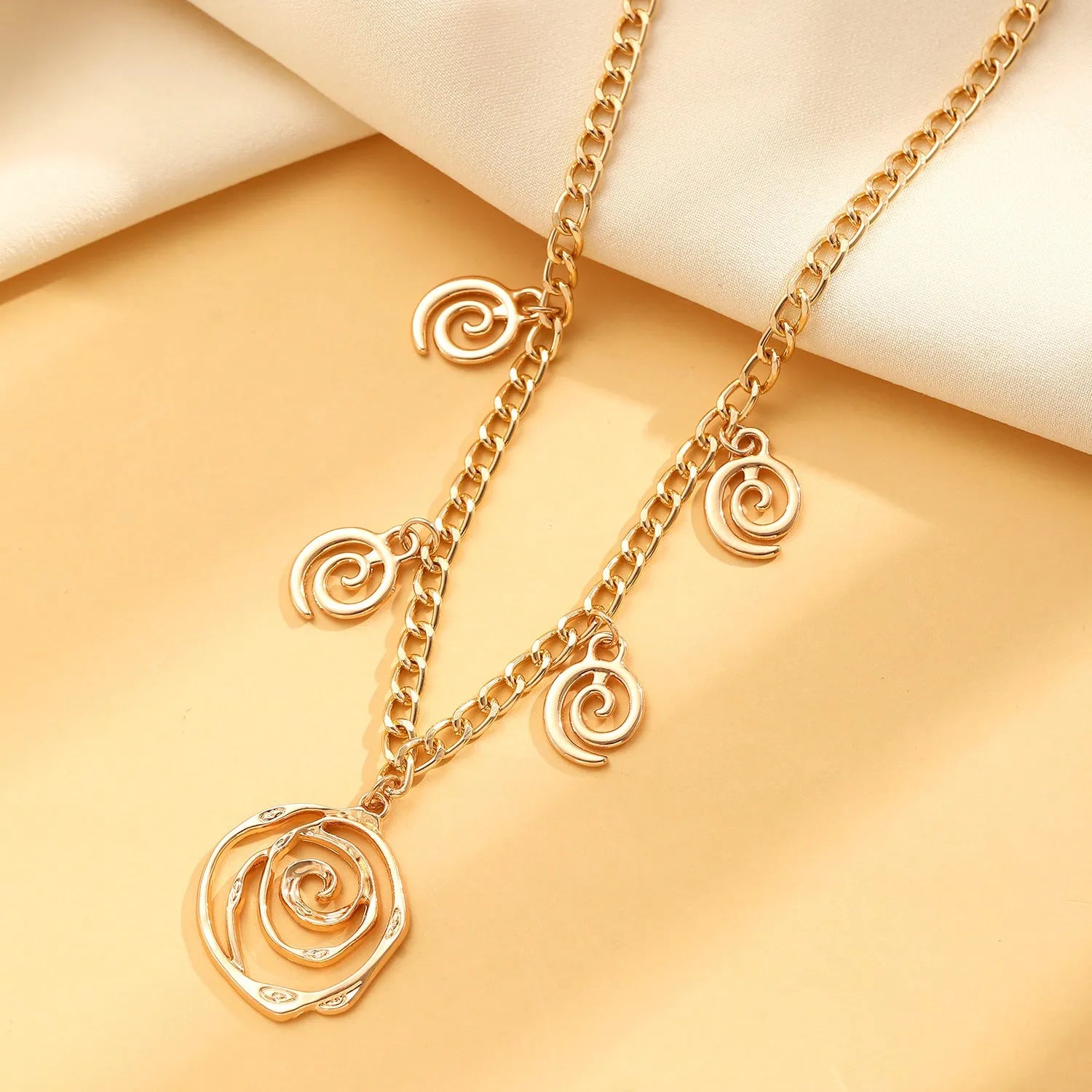 Gold spiral donut design necklace, bracelet, and earrings set on a grey background.