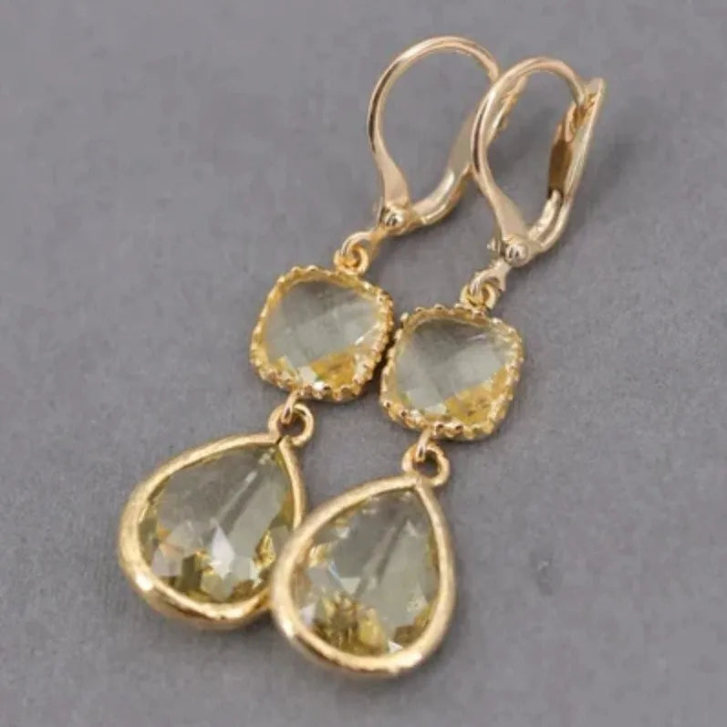Gold geometric long fringe drop earrings with water droplet design on a white background.