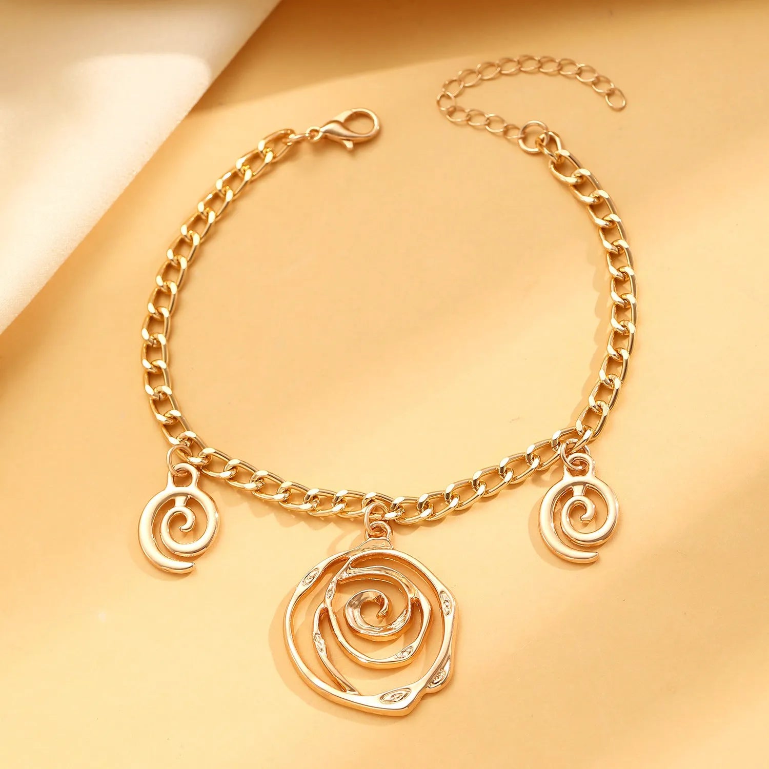 Gold spiral donut design necklace, bracelet, and earrings set on a grey background.