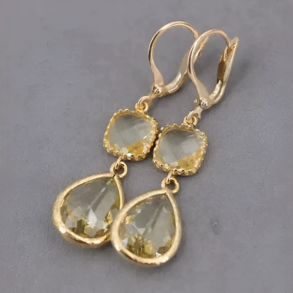 Gold geometric long fringe drop earrings with water droplet design on a white background.