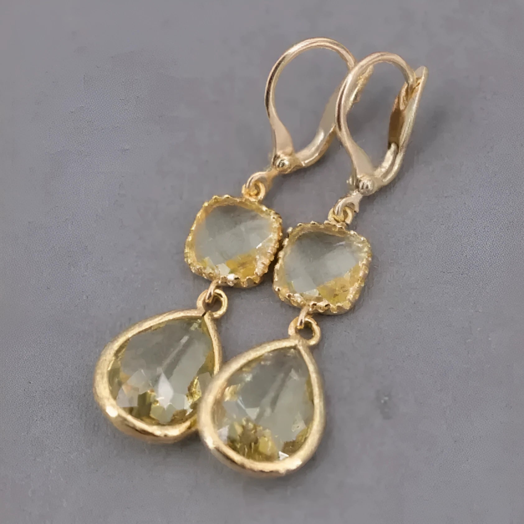 Gold geometric long fringe drop earrings with water droplet design on a white background.
