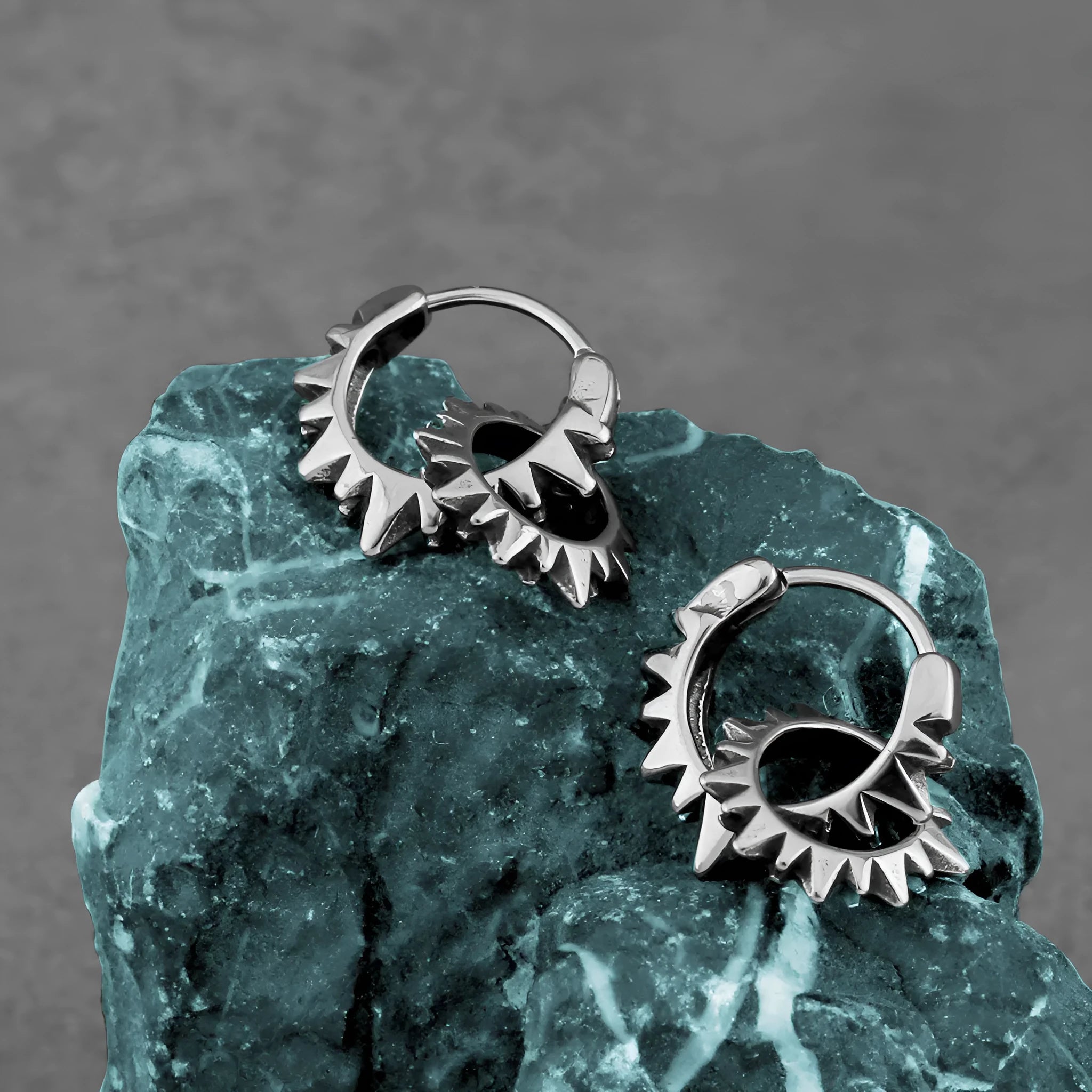 A pair of simple, polished stainless steel round ring earrings in a steel colour on a white background.