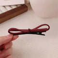 Close-up of a wine red leather bow barrette hair clip on dark hair.