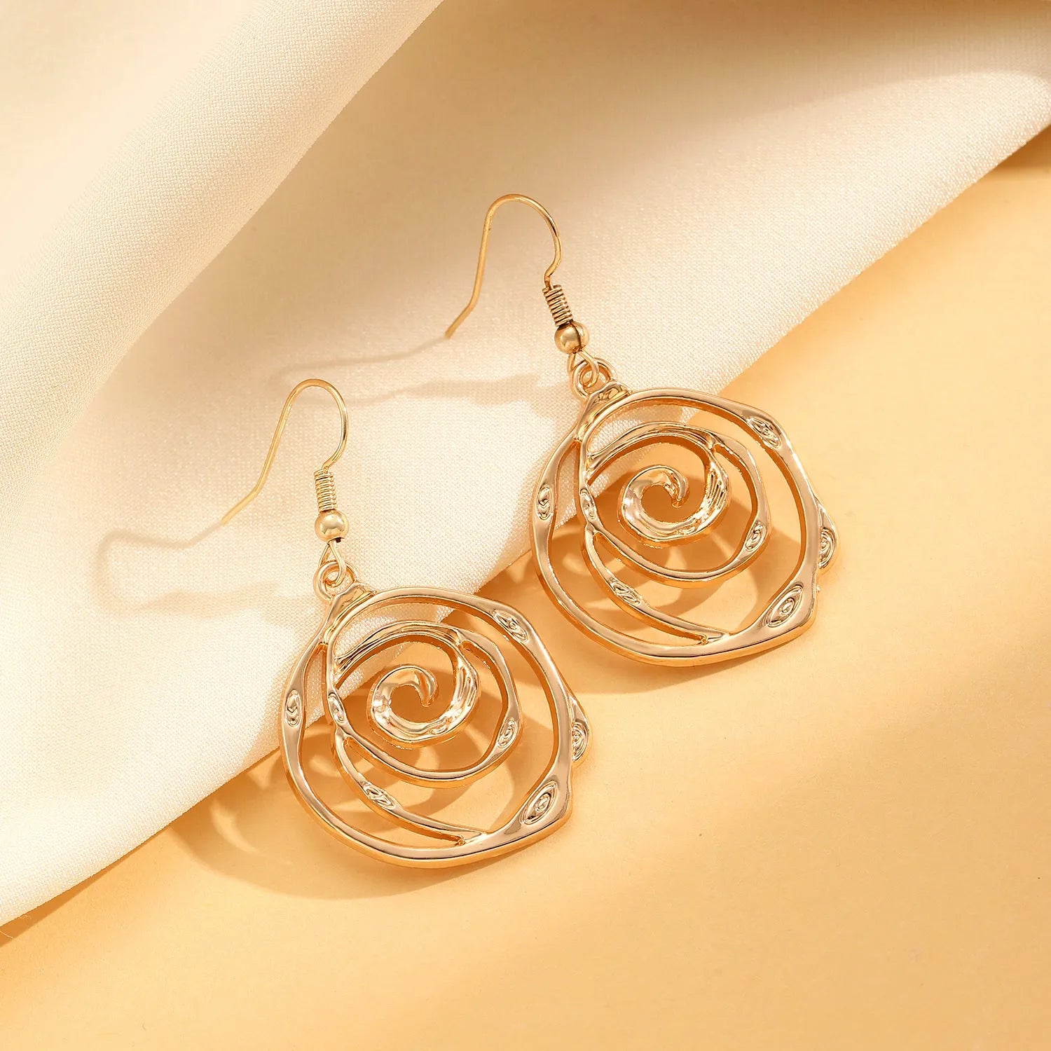 Gold spiral donut design necklace, bracelet, and earrings set on a grey background.