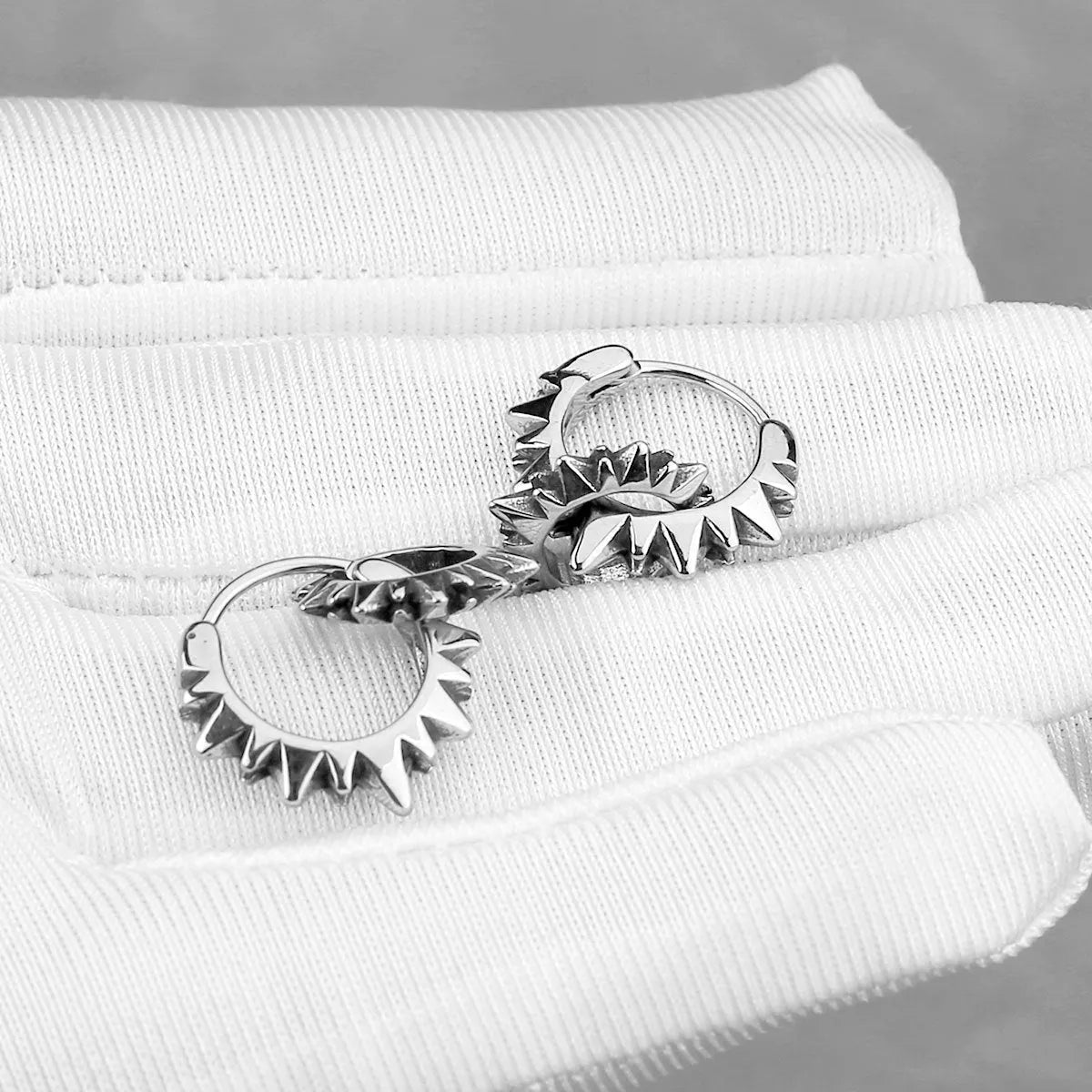 A pair of simple, polished stainless steel round ring earrings in a steel colour on a white background.