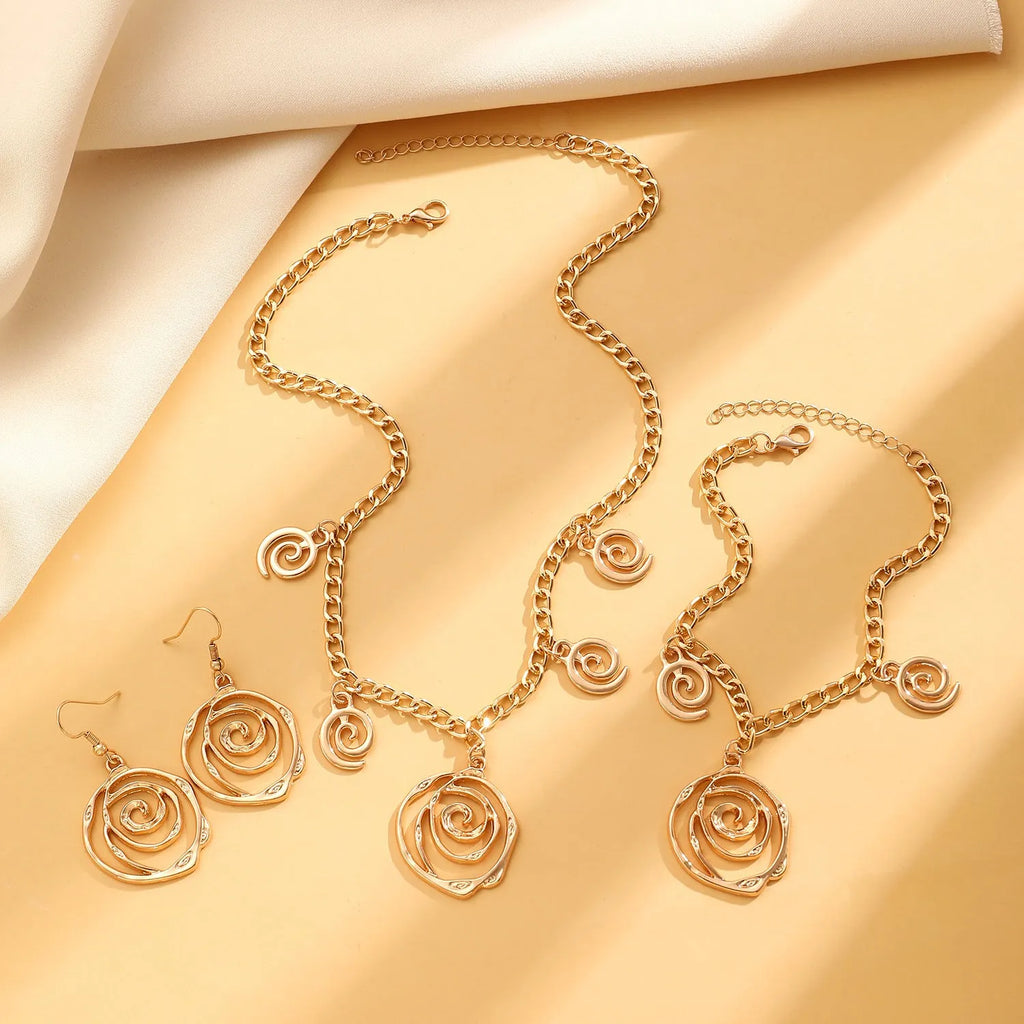 Gold spiral donut design necklace, bracelet, and earrings set on a grey background.
