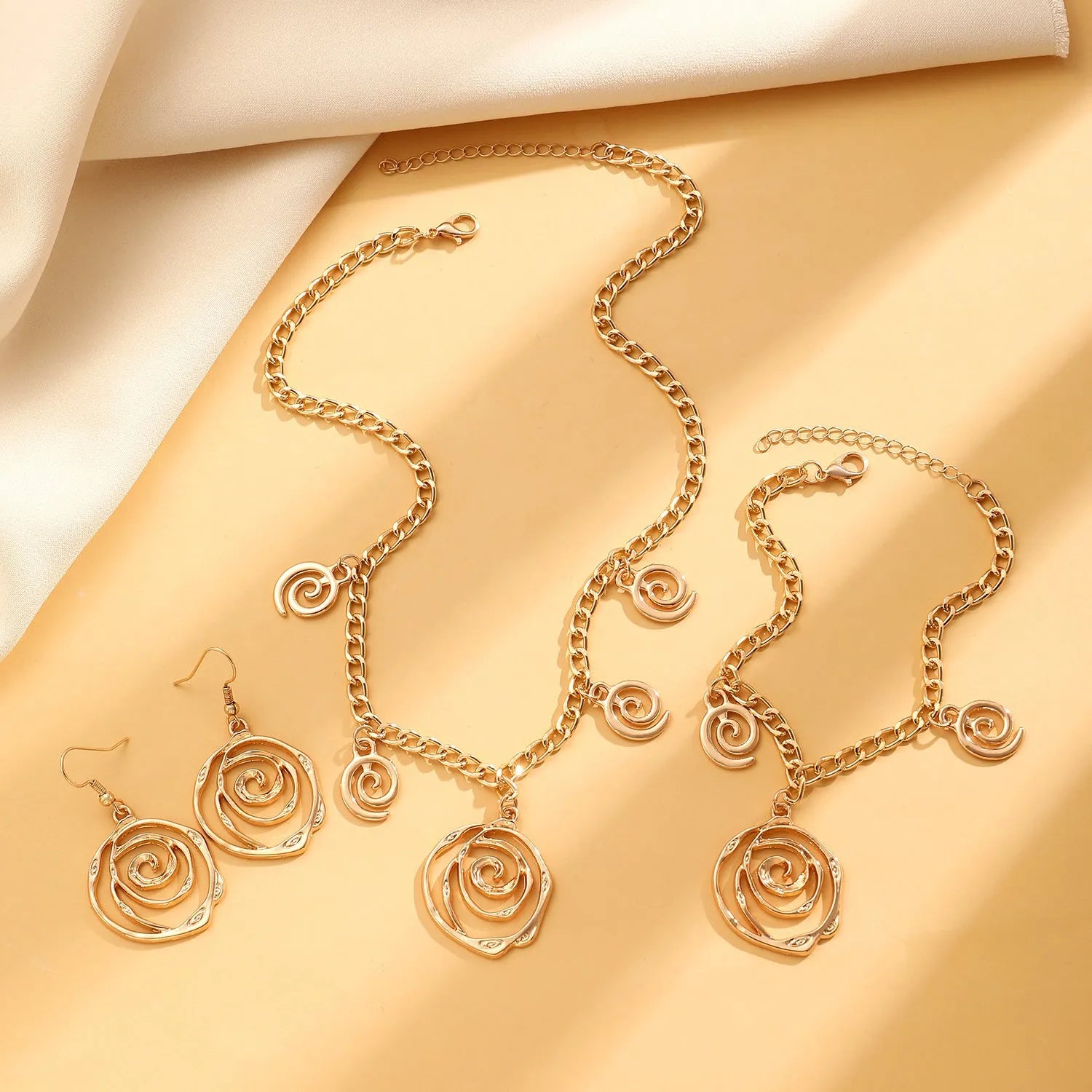 Gold spiral donut design necklace, bracelet, and earrings set on a grey background.