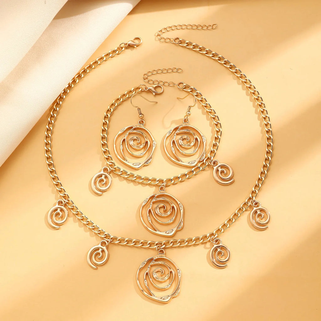 Gold spiral donut design necklace, bracelet, and earrings set on a grey background.
