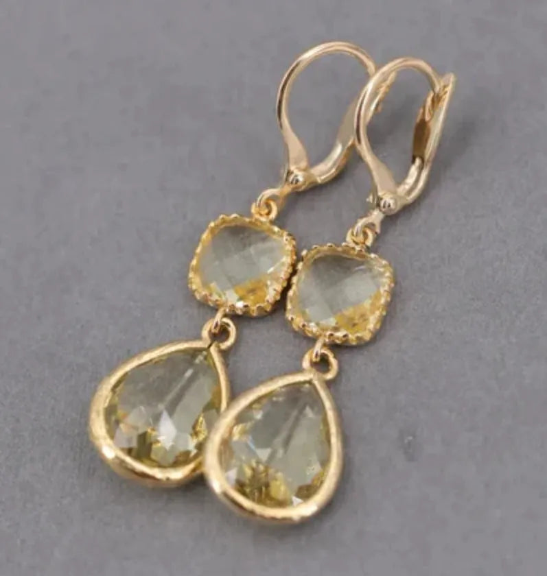 Gold geometric long fringe drop earrings with water droplet design on a white background.