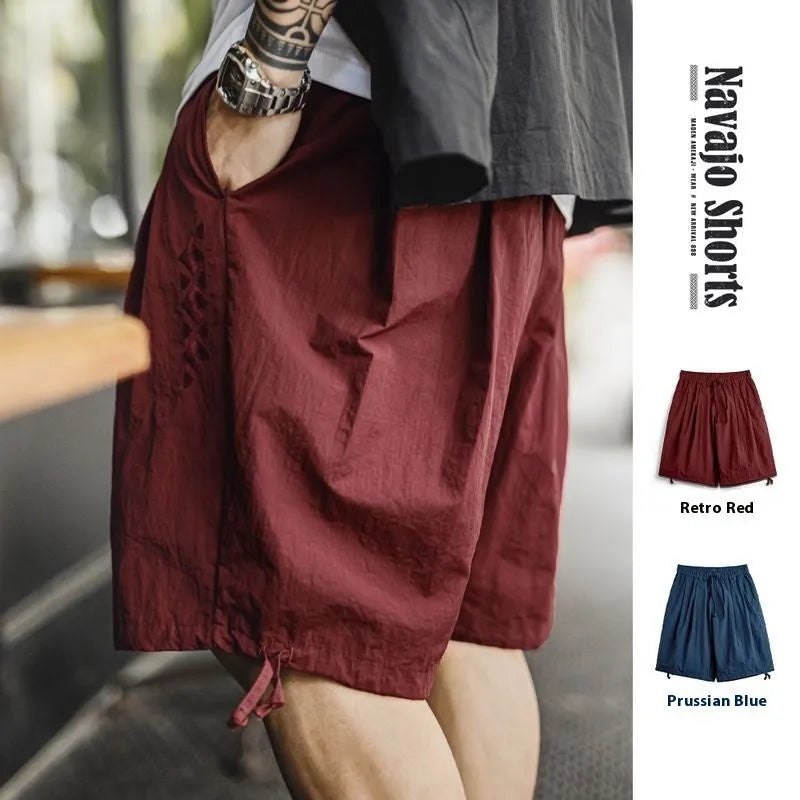 Men's loose fit Prussian Blue nylon beach shorts with embroidery on a summer background.