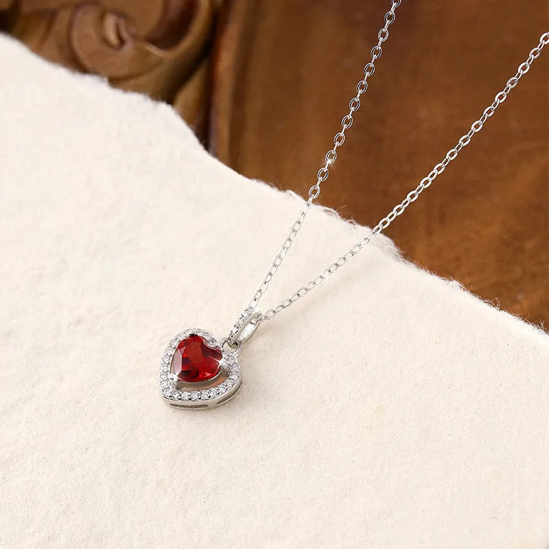 Close-up of a sterling silver heart necklace with an inlaid amethyst gemstone on a cross chain.