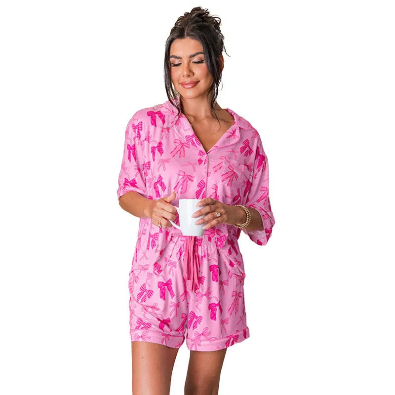 Pink women's two-piece pajama set with bow print, featuring a top and matching trousers.