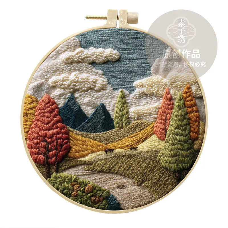 DIY embroidery kit with landscape-printed cotton fabric, embroidery hoop, needles, and coloured thread spools.