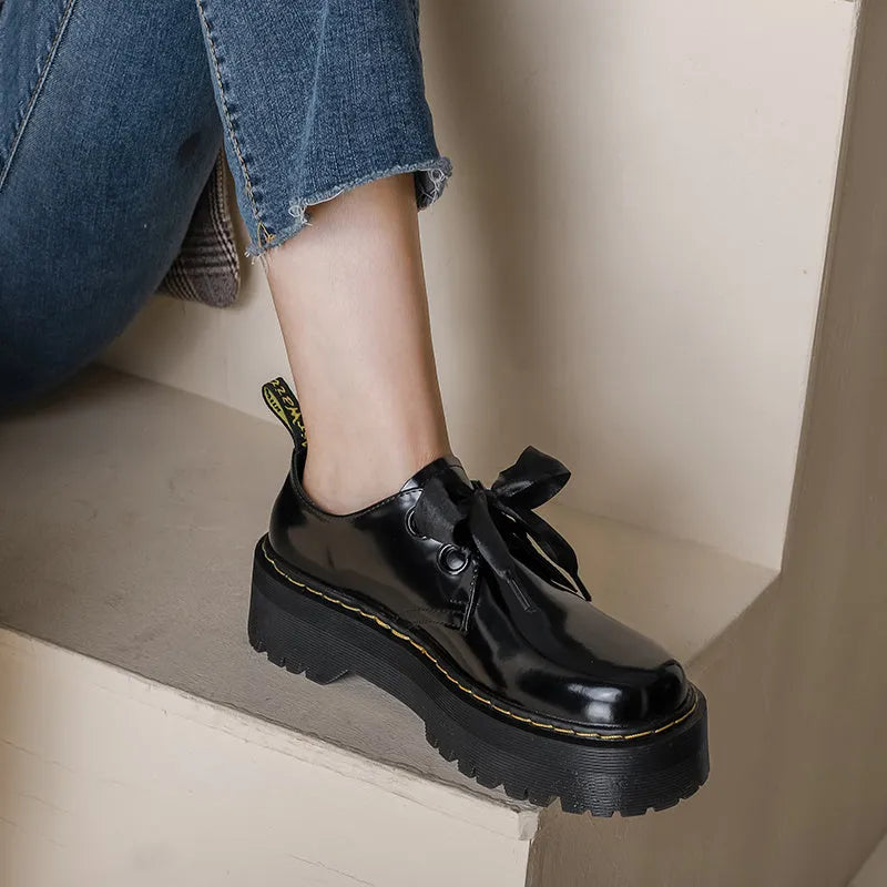Black thick-soled women's lace-up shoes with ribbon and cross strap detailing on a white background