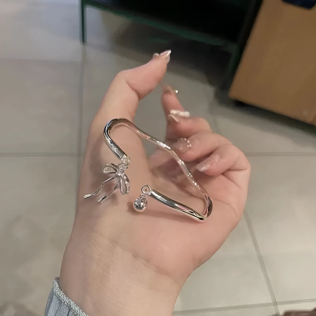 Silver adjustable bracelet with a fixed bow charm on a wrist.