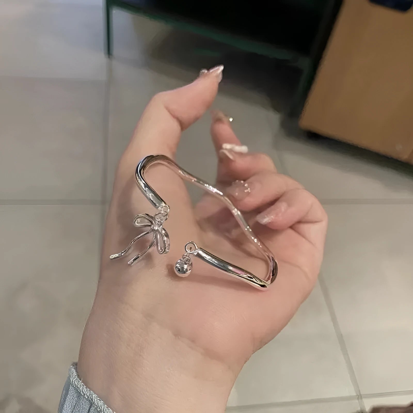 Silver adjustable bracelet with a fixed bow charm on a wrist.
