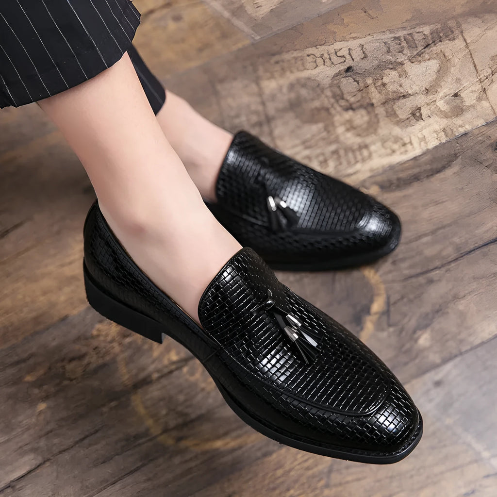 Men's black pointed toe slip on shoes with a gold tassel detail on the upper.