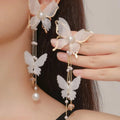 Close-up of white butterfly-shaped earrings with dangling lace tassels, pearl beads, and clear rhinestone accents.