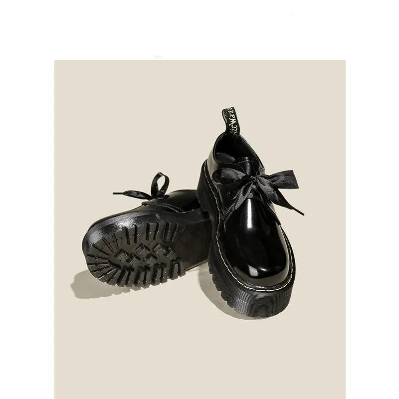Black thick-soled women's lace-up shoes with ribbon and cross strap detailing on a white background