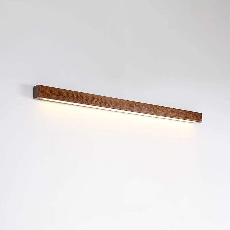 Walnut colour minimalist wooden and acrylic strip wall lamp in three length options on a white wall.