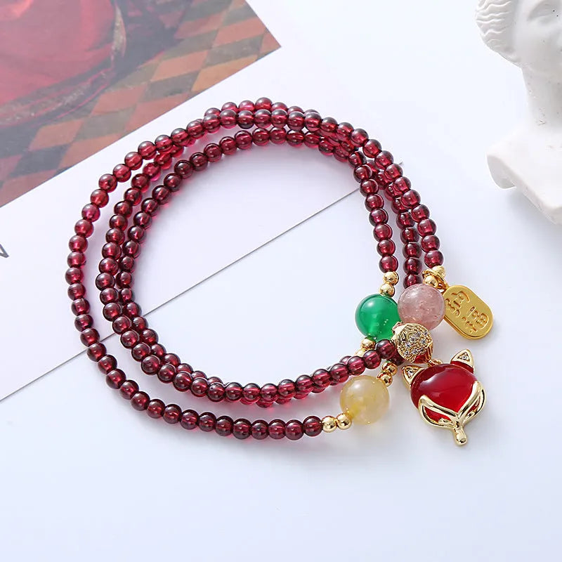 Purplish red garnet fox charm bracelet with adjustable rope on a wrist.