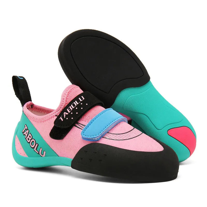 Beginner rock climbing shoes with Velcro strap in black and red colour scheme on a rocky surface.