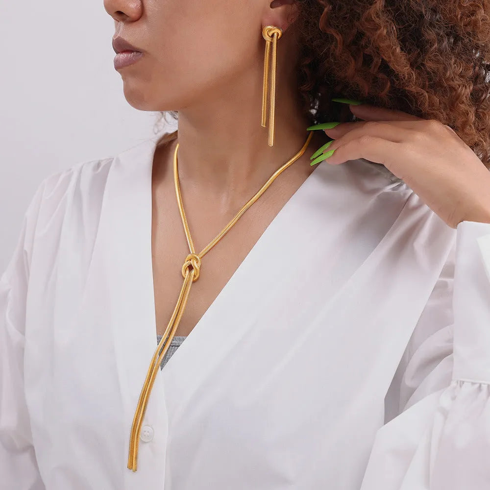 Gold titanium steel long necklace with knotted tassel pendant and matching earrings on a white background.