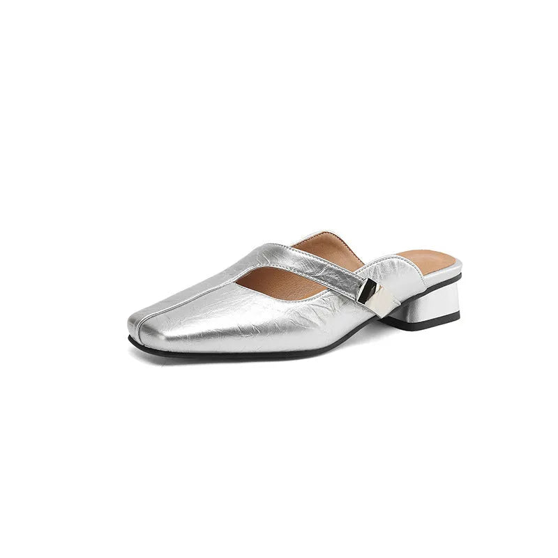 A pair of beige square head low heel slippers with a rubber sole on a wooden deck.