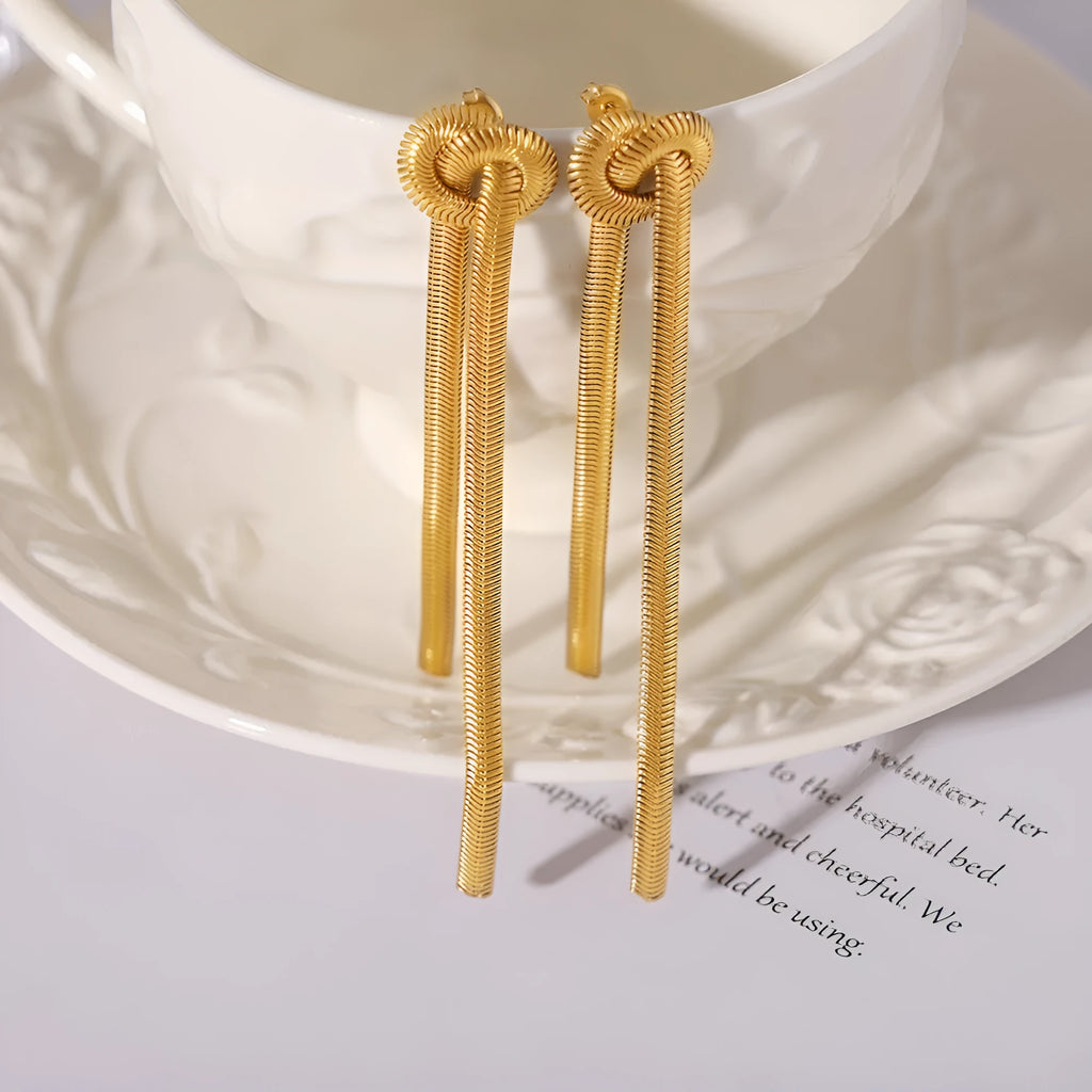 Gold titanium steel long necklace with knotted tassel pendant and matching earrings on a white background.