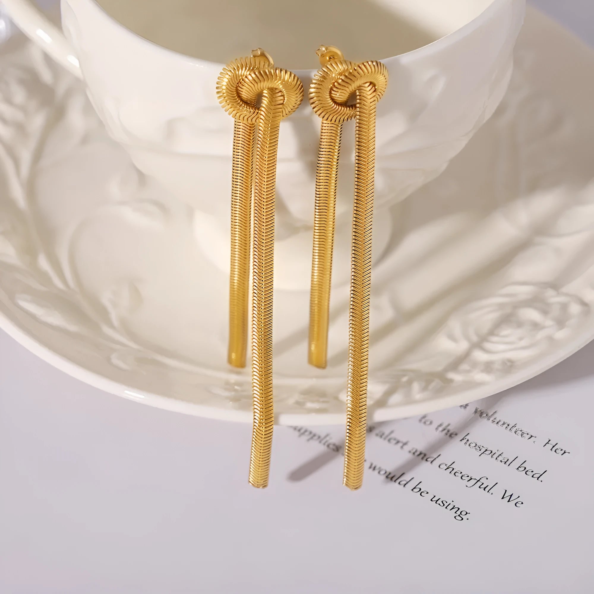 Gold titanium steel long necklace with knotted tassel pendant and matching earrings on a white background.