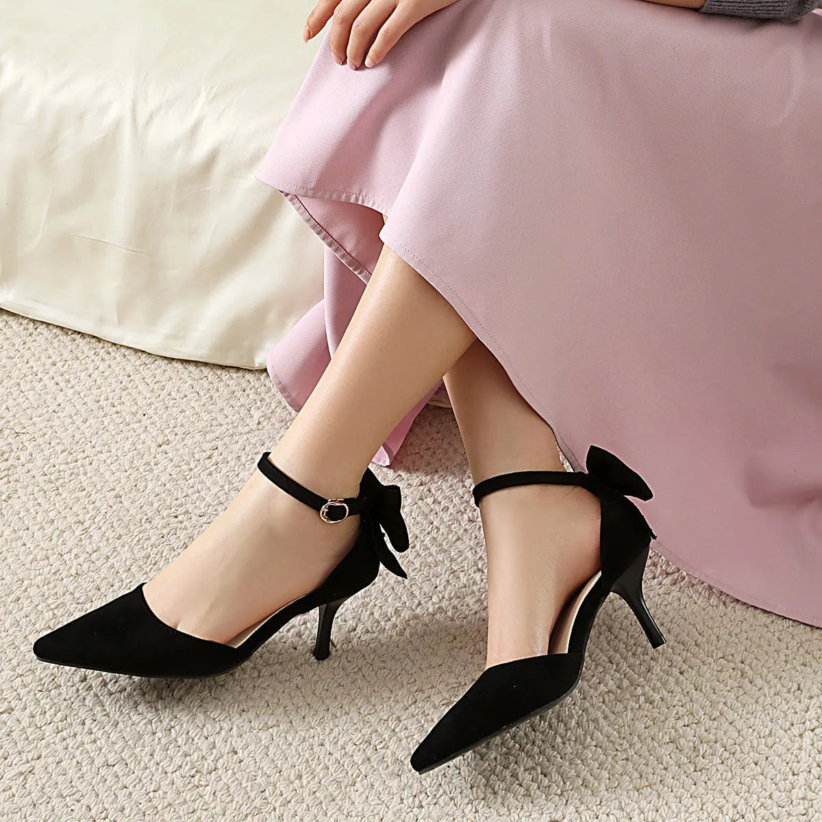 A pair of black suede stiletto high heels with a pointed toe and an ankle buckle.
