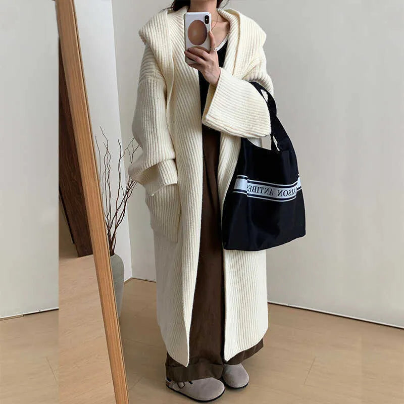 A long, loose grey hooded cardigan coat for women on a hanger, showing its length and raglan sleeves.