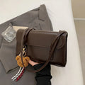 Brown women's square PU shoulder bag with a detachable pendant on a table