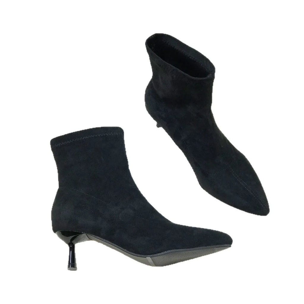 Black pointed toe stiletto ankle boots with a mid-calf sock length on a model.