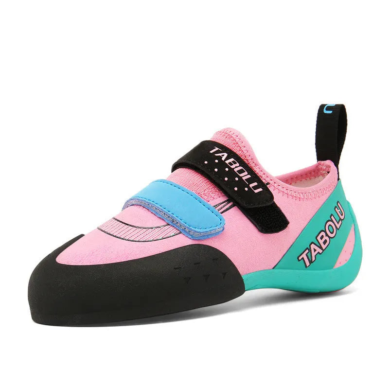 Beginner rock climbing shoes with Velcro strap in black and red colour scheme on a rocky surface.