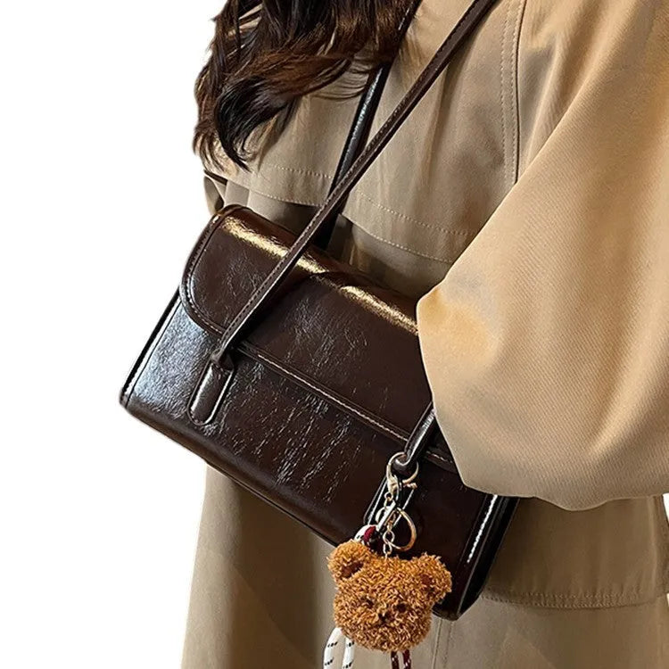 Brown women's square PU shoulder bag with a detachable pendant on a table