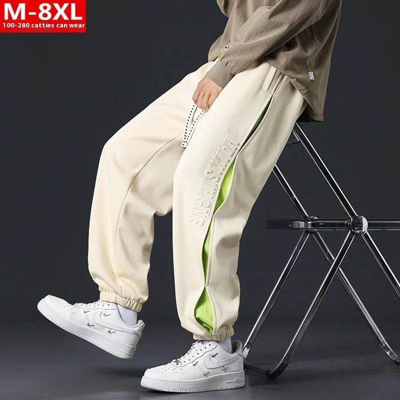 Man wearing loose grey-green cotton trousers with banded ankles and stitching detail.