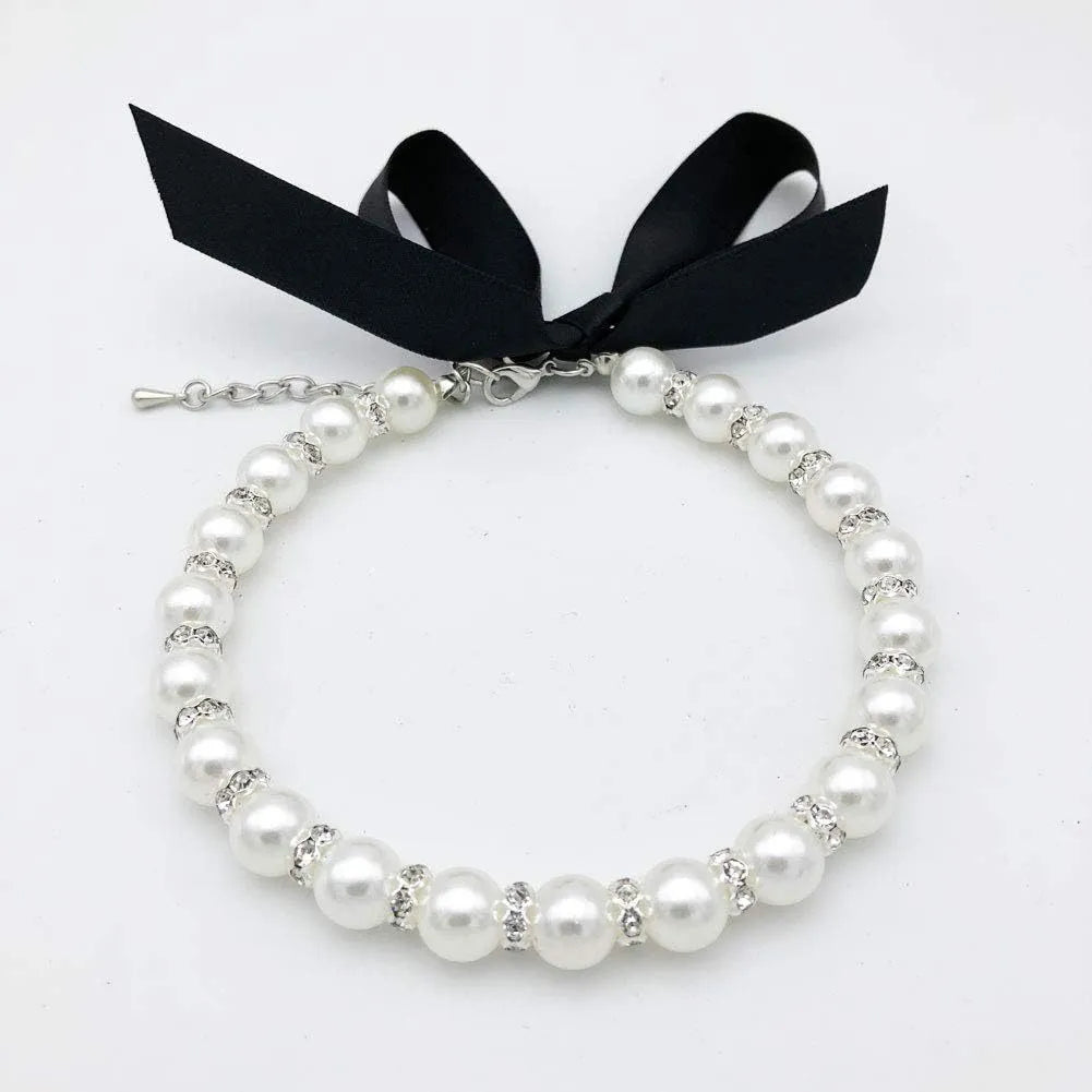 Small dog wearing an adjustable blue pearl and rhinestone necklace with a ribbon bow.