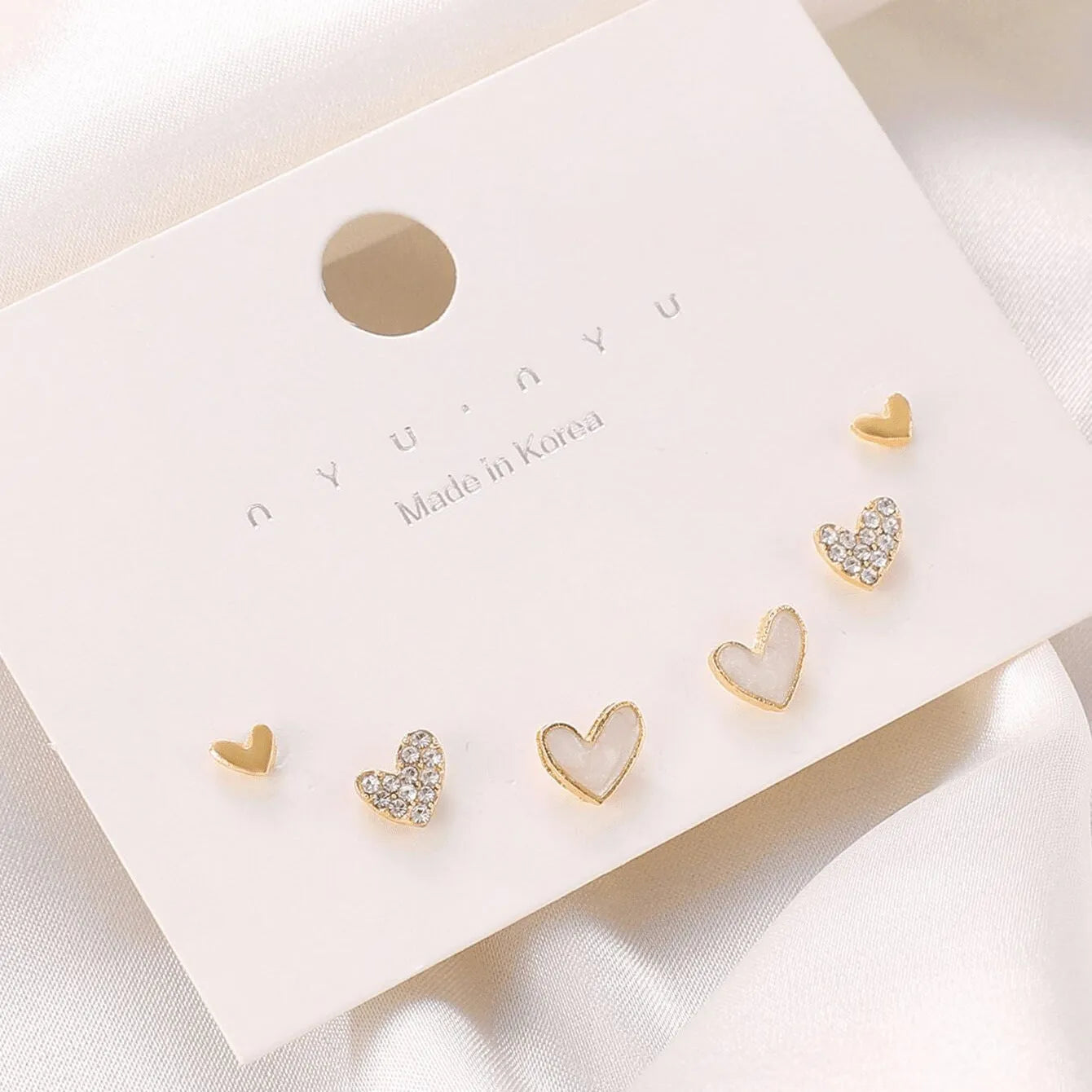 Three pairs of heart-shaped alloy earrings in gold, black, black and white, and pink colours