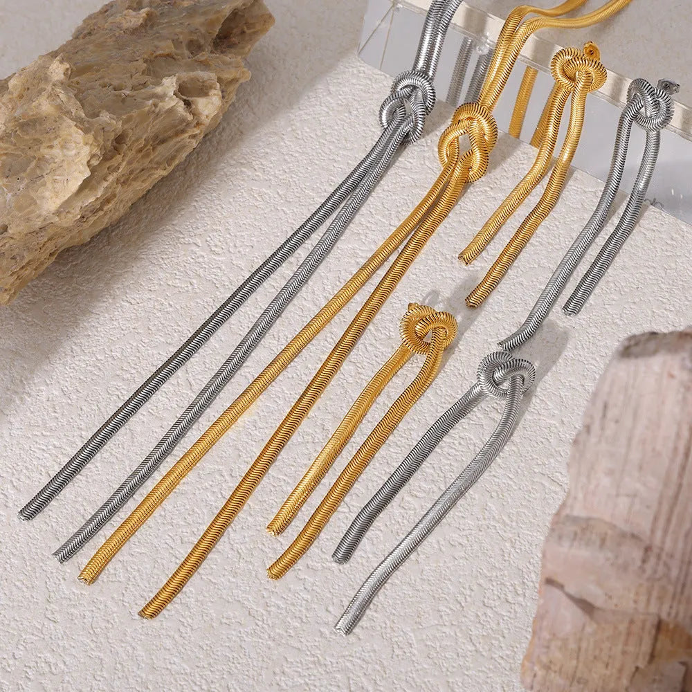 Gold titanium steel long necklace with knotted tassel pendant and matching earrings on a white background.