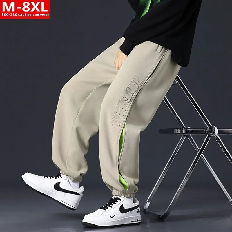 Man wearing loose grey-green cotton trousers with banded ankles and stitching detail.