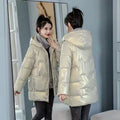 A green loose-fit hooded winter jacket for women on a hanger, showing long sleeves and thick insulation.