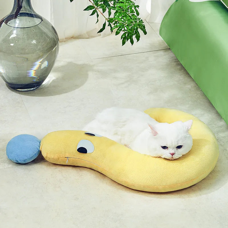 A rectangular blue pet sleeping pillow on a floor, shown next to a small dog for scale.