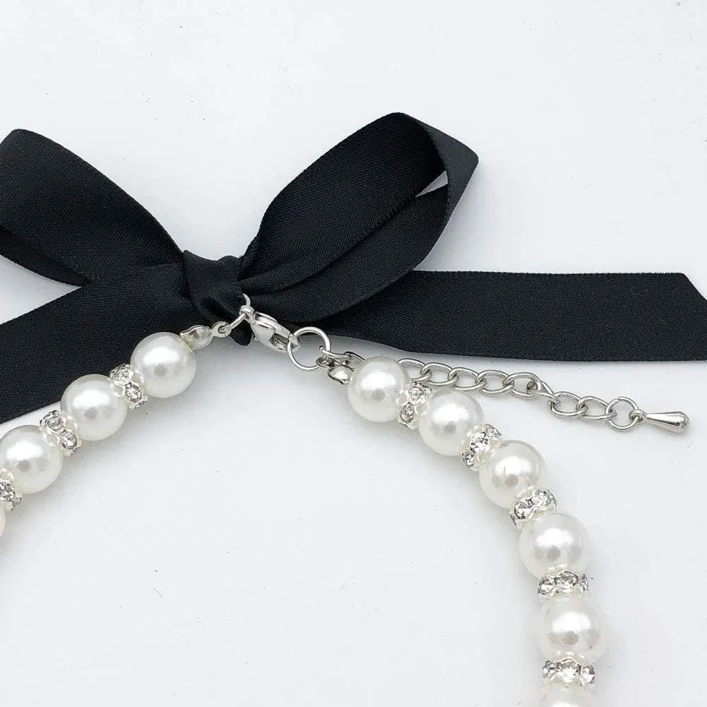 Small dog wearing an adjustable blue pearl and rhinestone necklace with a ribbon bow.