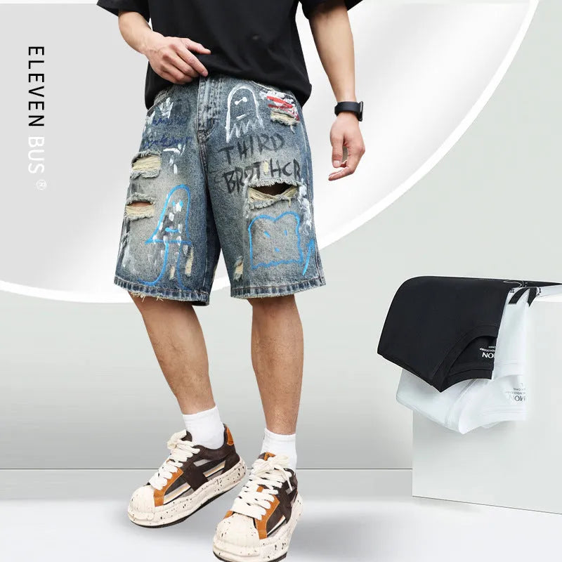Blue men's ripped denim shorts with a graffiti pattern and zipper fly, laid flat.