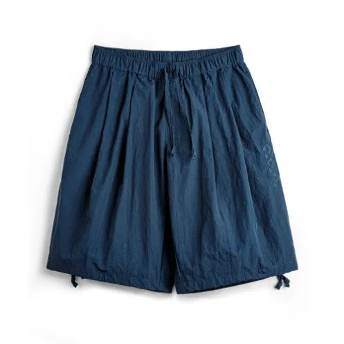 Men's loose fit Prussian Blue nylon beach shorts with embroidery on a summer background.