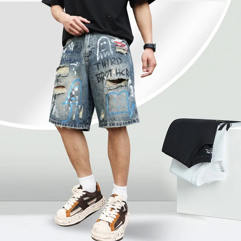 Blue men's ripped denim shorts with a graffiti pattern and zipper fly, laid flat.