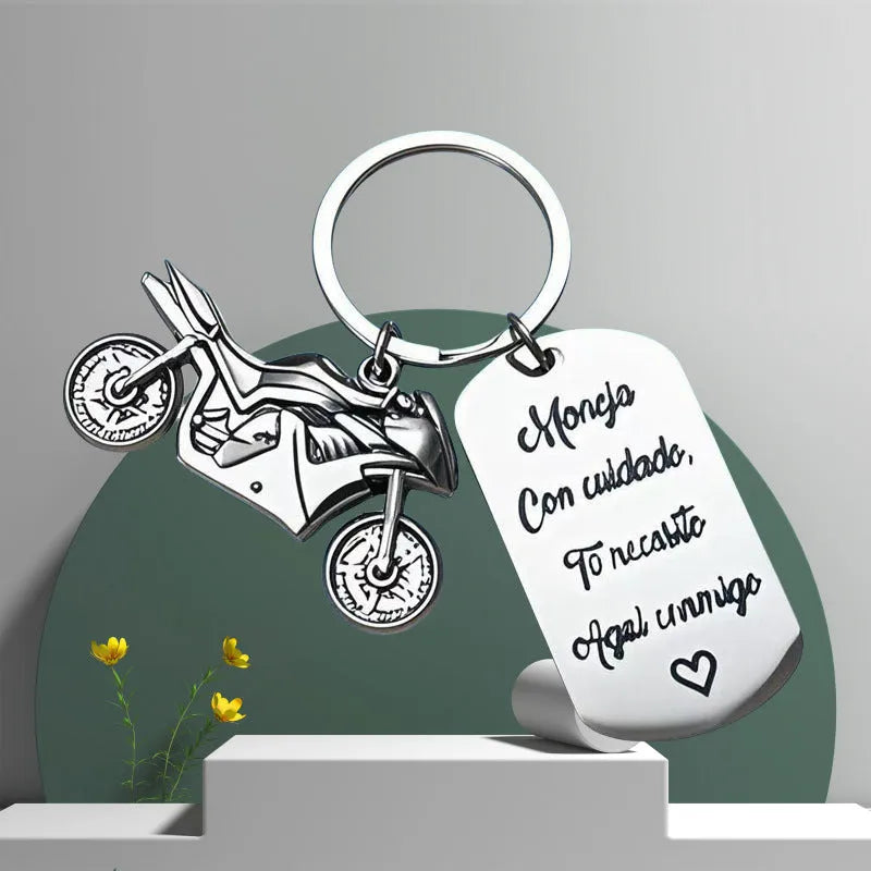 Polished stainless steel motorcycle key ring with inspirational charm on a flannel bag.